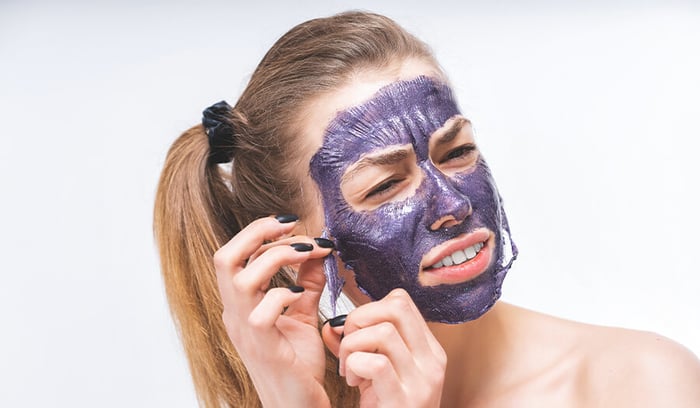 a_young_girl_with_a_beautiful_face_with_difficulty_removes_a_purple_cosmetic_mask
